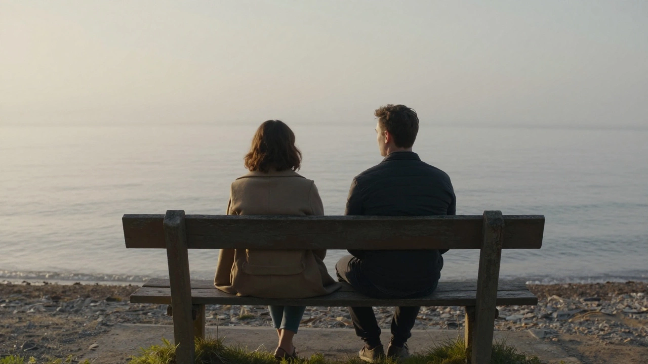 Two people sitting in silent companionship on a seaside bench at sunrise, facing the ocean.